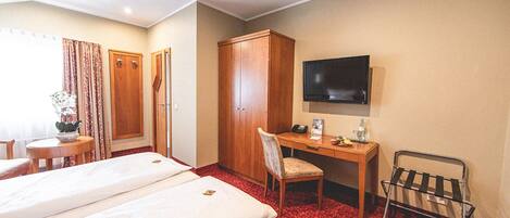 A hotel room with two beds, a desk, a chair, a TV, and a wardrobe.