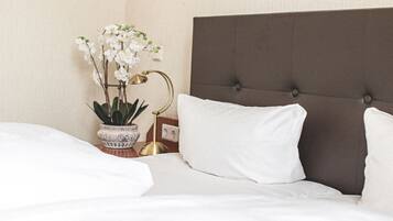Un lit bien fait, avec une literie blanche, une tête de lit marron recouverte de tissu et une orchidée en pot posée sur la table de chevet.