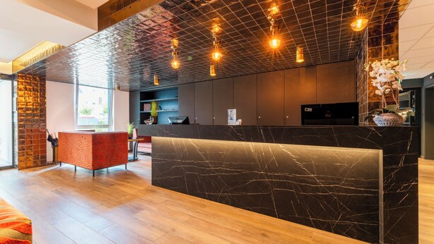 Un moderno mostrador de recepción con encimera de mármol, suelo de madera y techo con diseño de cuadrícula y luces colgantes.