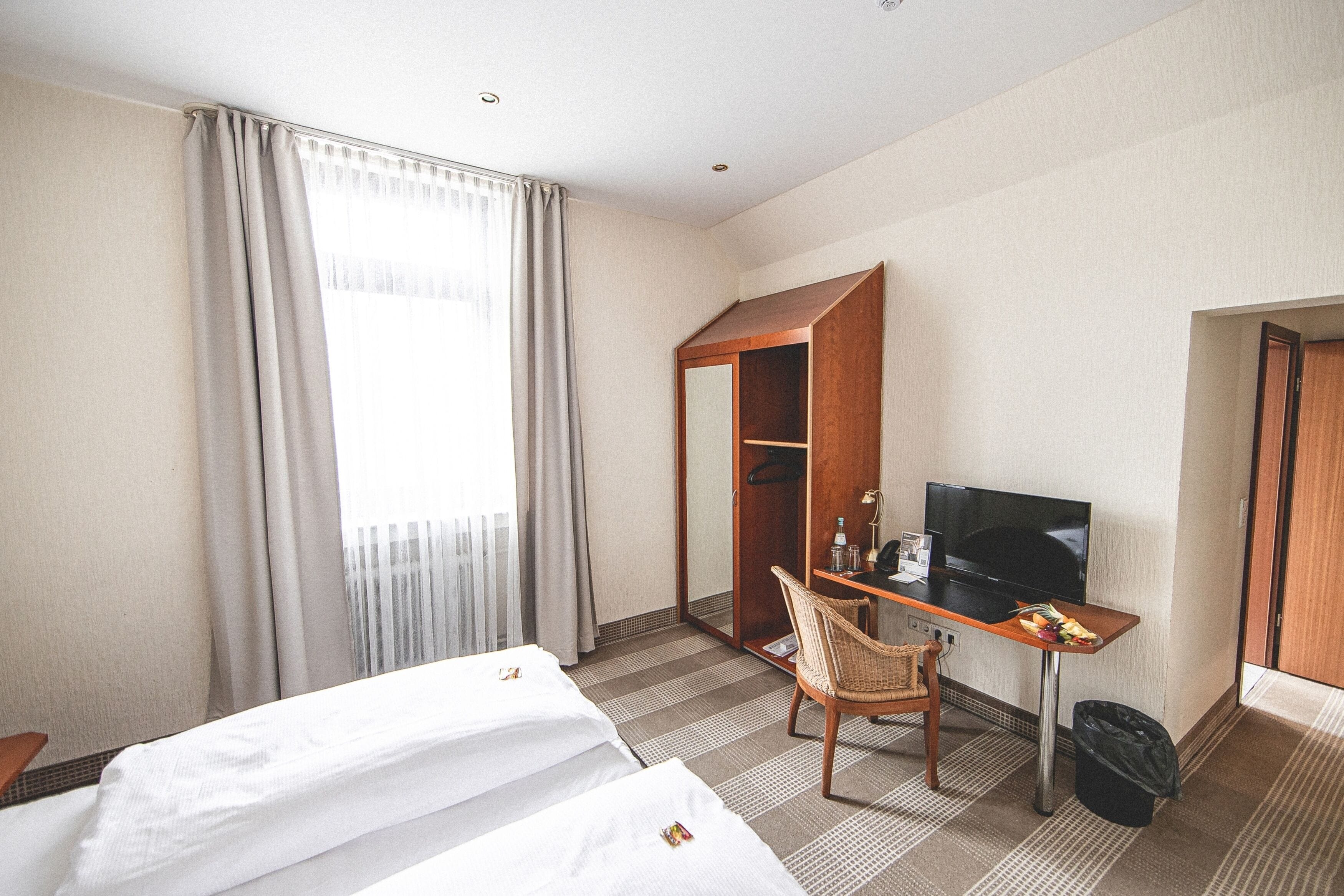 A hotel room with two beds, a desk with a TV, a chair, and a wardrobe.