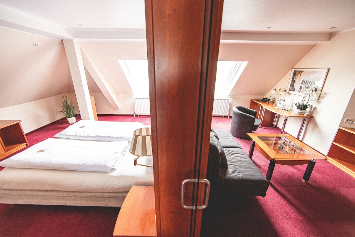 Una habitación con una cama, un sofá, una mesa de madera y un escritorio con una lámpara.