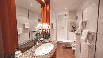 A modern bathroom with a granite countertop sink, a large mirror, and a glass shower enclosure.