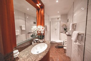 Une salle de bain moderne avec un lavabo surmonté d’un plan de travail en granit, un grand miroir et une douche à parois de verre.