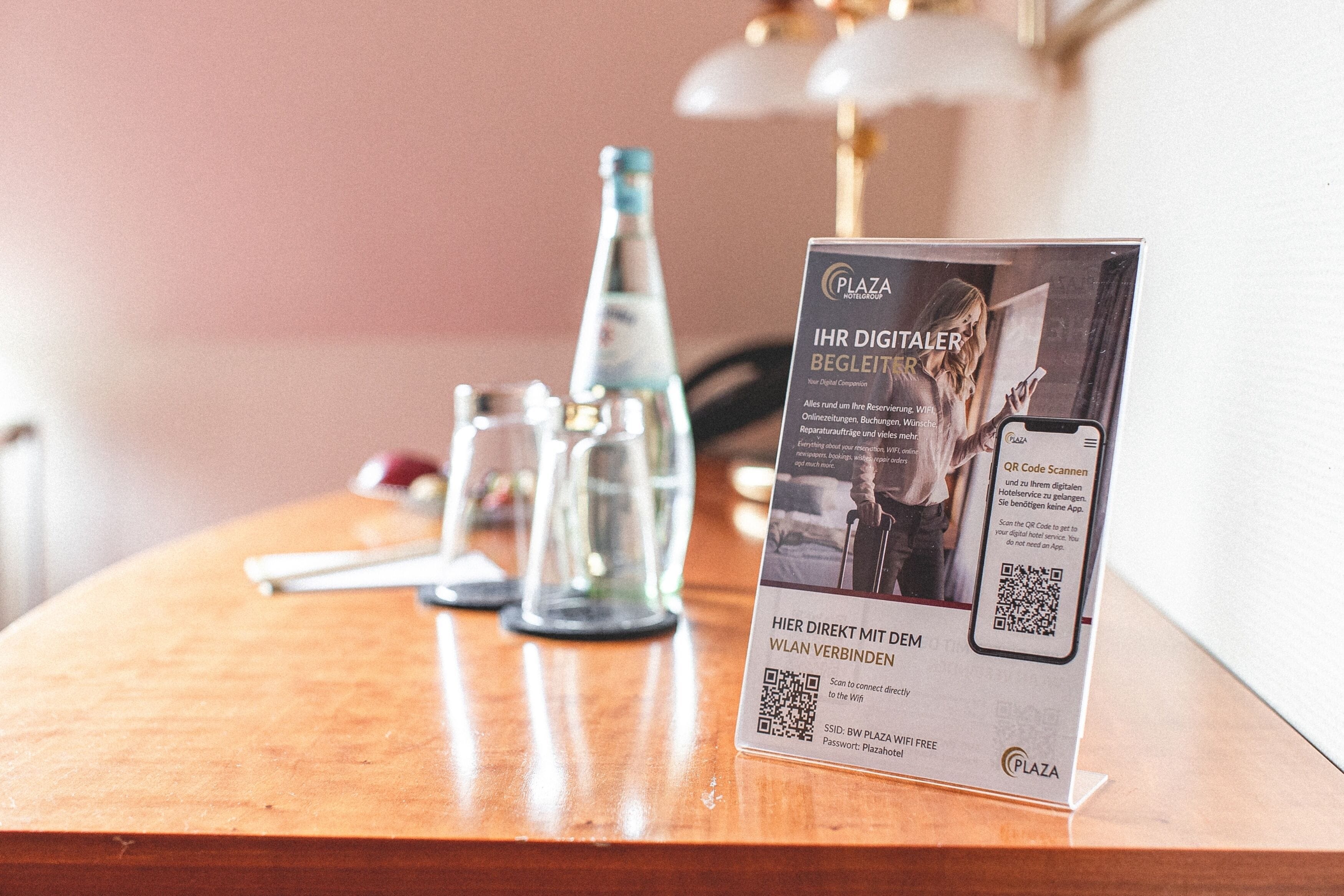 Balcão de recepção de hotel com um sinal de código QR para serviços digitais, uma garrafa de água e um copo.