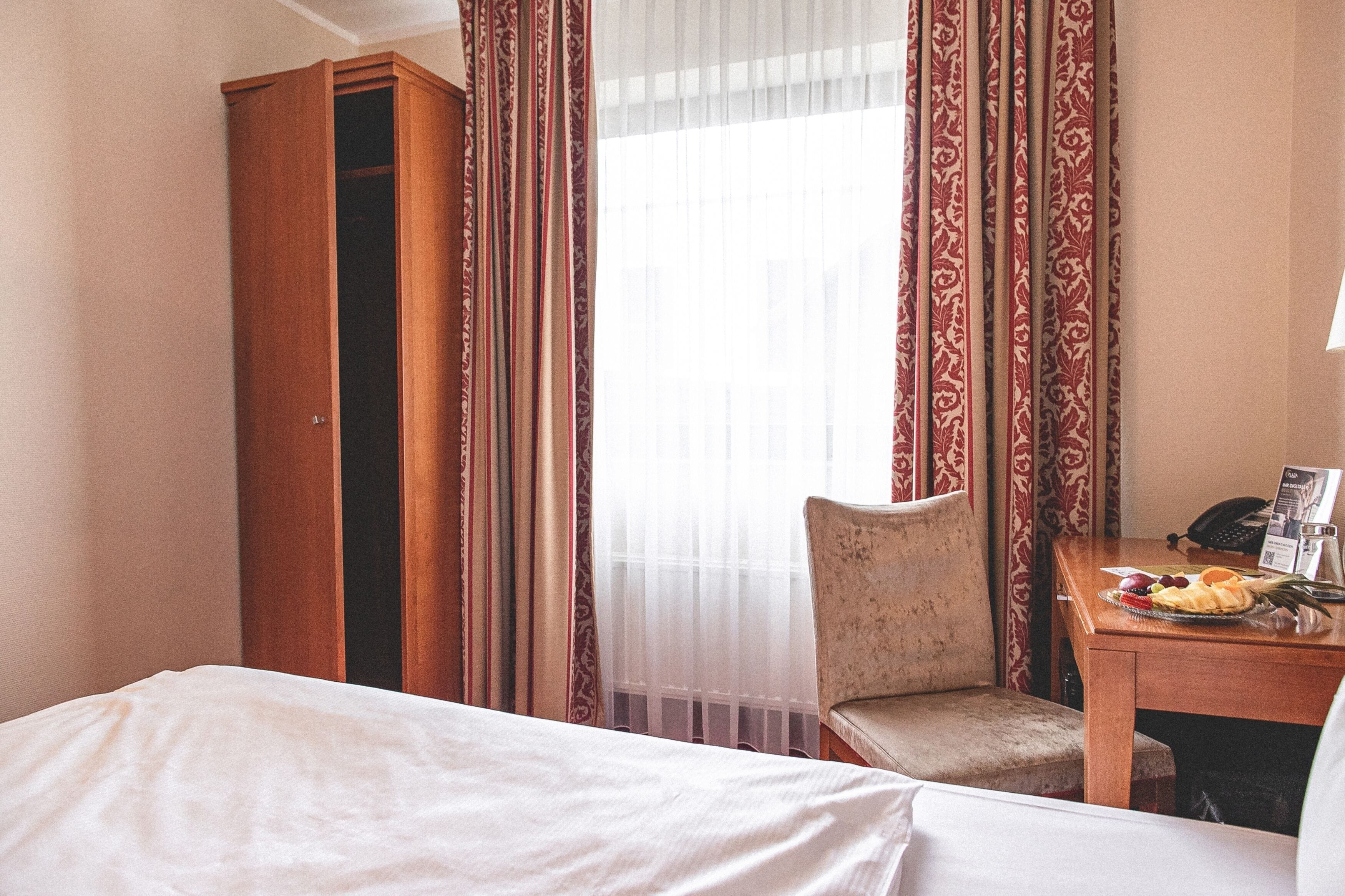 A hotel room with a bed, a chair, a small table with a plate of fruit, and a telephone.