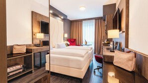 Una habitación de hotel moderna con una cama grande, un escritorio con silla, un televisor y un armario.