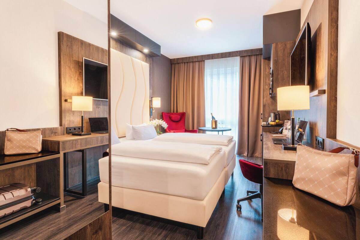 Una habitación de hotel moderna con una cama grande, un escritorio con silla, un televisor y un armario.