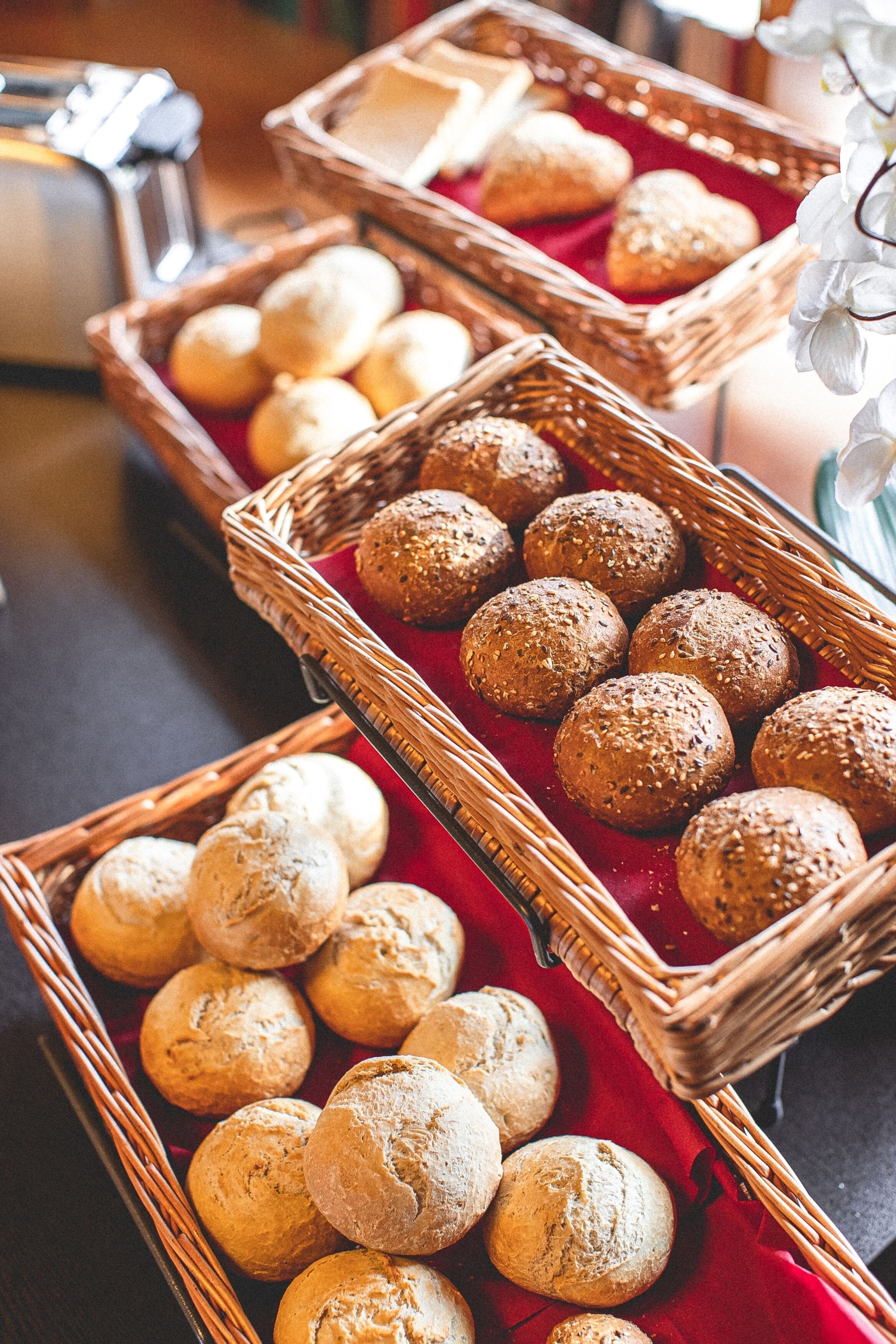 Three wicker baskets filled with various types of bread on a red cloth.