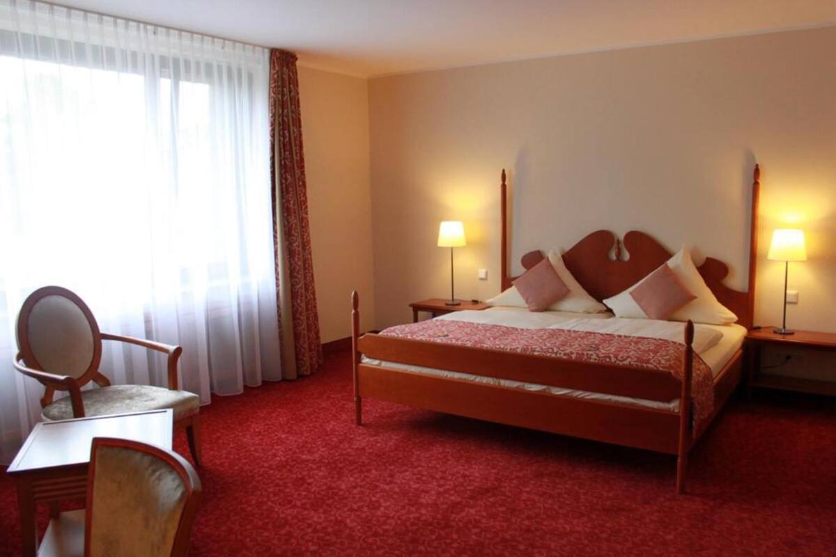 Una habitación de hotel con una cama de madera, dos lámparas de noche, una silla y una mesa.