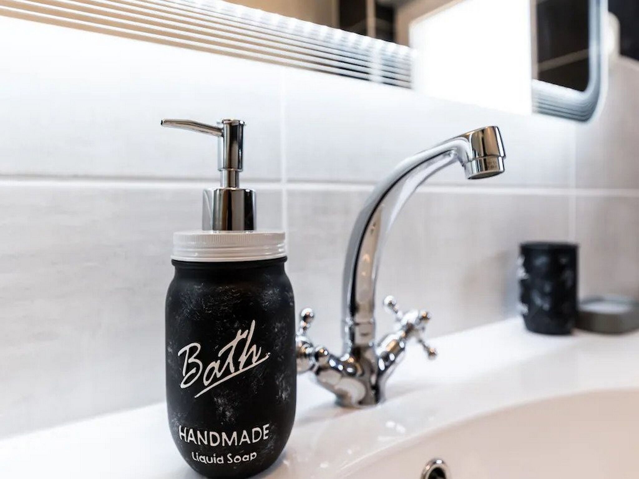 Une salle de bain avec un distributeur de savon noir portant l’étiquette « Savon liquide artisanal pour le bain » et un robinet chromé.