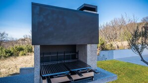 Un barbecue d’extérieur moderne, doté d’une surface de cuisson plane et d’un thermomètre intégré, se dressant sur un ciel dégagé et entouré d’une pelouse bien entretenue.