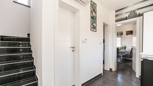 Un intérieur moderne avec un escalier, une porte blanche et un couloir menant à une salle à manger.