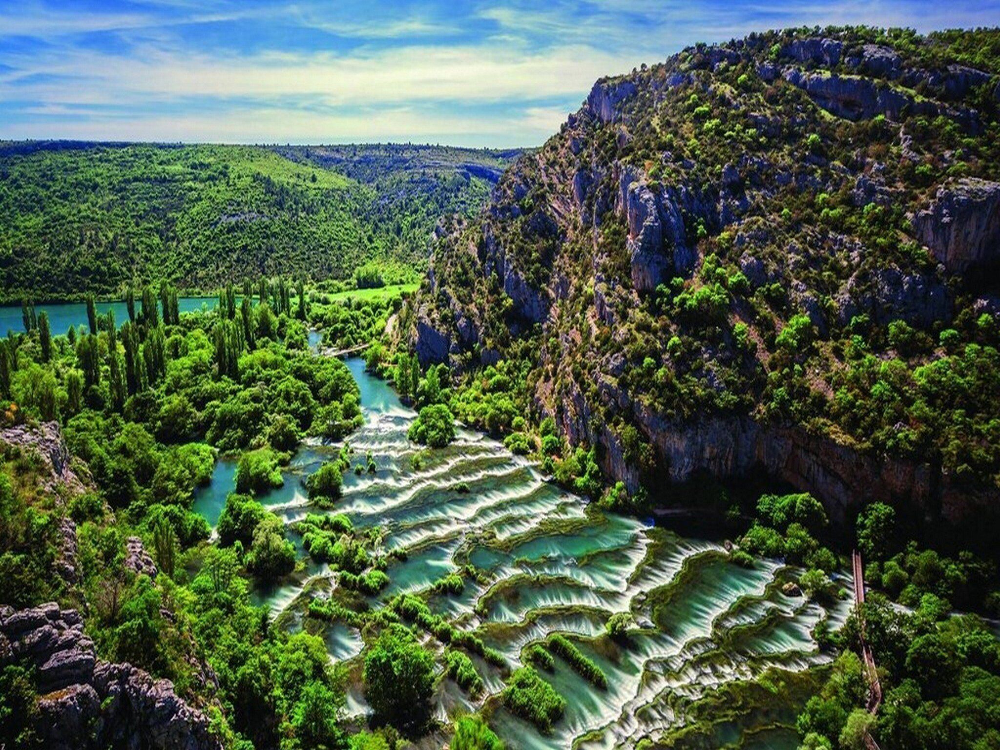 A natural landscape with terraced water formations and dense greenery.