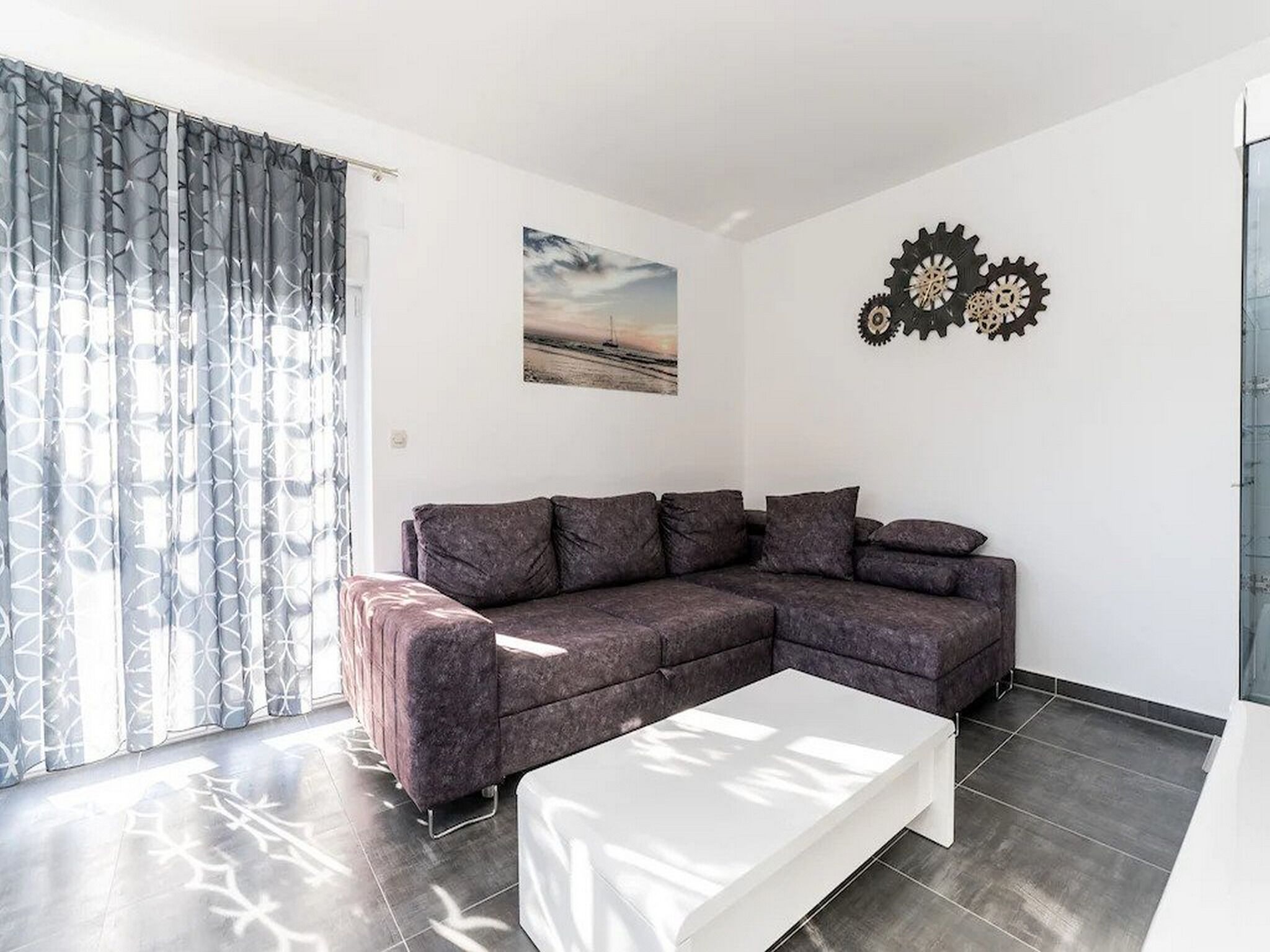 A modern living room with a sectional sofa, a white coffee table, and a large window with patterned curtains.