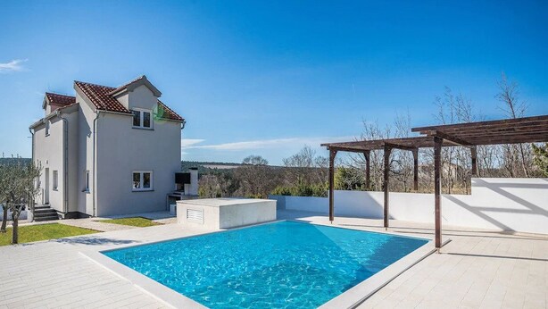 Une maison moderne dotée d’une piscine, d’une pergola et offrant une vue sur la campagne.