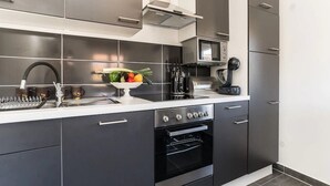 Une cuisine moderne avec des meubles de couleur sombre, une hotte de cuisine en acier inoxydable, un four à micro-ondes et un four traditionnel.