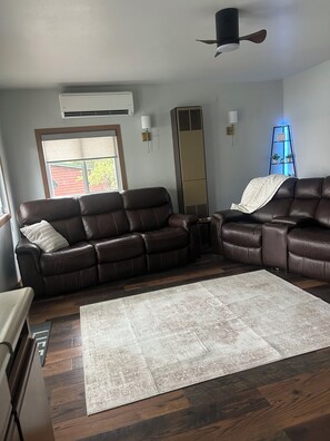 A living room with a brown leather sofa, a white rug, and a ceiling fan.