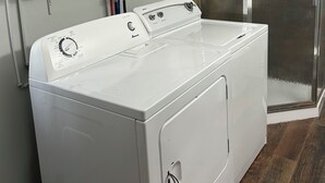 A laundry room with a front-loading washer and dryer, shelves with folded towels, and a glass shower enclosure. - Cottage on The Lake (Redfield)