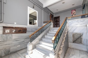 A marble staircase with a wooden handrail, a wall-mounted mirror, and a door with a poster.