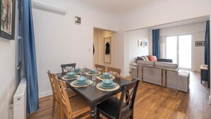 Een eetruimte met een tafel gedekt voor vier personen, een bank en een raam met gordijnen.
