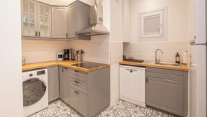 Een kleine keuken met grijze kastjes, een wasmachine, een vaatwasser en een houten aanrecht.