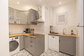 A compact kitchen with grey cabinets, a washing machine, a dishwasher, and a wooden countertop.