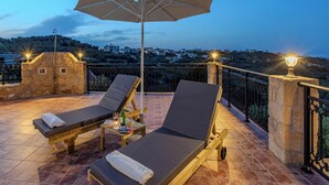 Una terrazza con due lettini, un tavolo con bevande e un ombrellone.