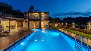 Una casa a due piani con piscina, area salotto esterna e un muro in pietra.