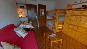 Habitación compacta con sofá rojo, una mesita, literas y un escritorio con lámpara.