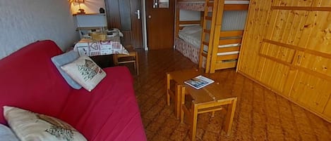 A compact room with a red sofa, a small table, a bunk bed, and a desk with a lamp.