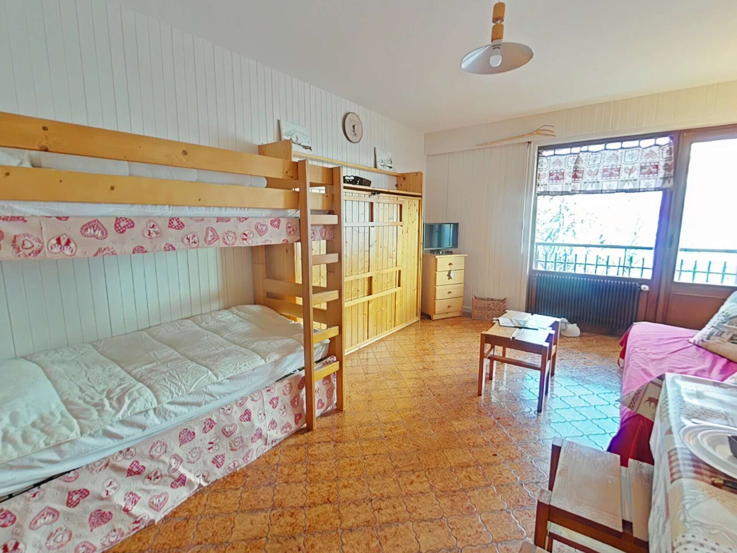 A room with bunk beds, a desk, a chair, a wardrobe, and a window with a view.