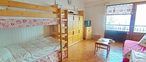 A room with bunk beds, a desk, a chair, a wardrobe, and a window with a view.