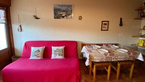 Una habitación acogedora con un sofá rojo, una mesa de comedor dispuesta para cuatro comensales y un cuadro colgado en la pared.