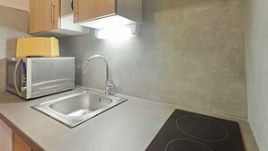 Una cocina con un lavamanos de acero inoxidable, un tostador y un microondas. Hay un armario de madera sobre la encimera y una lámpara sobre el lavamanos.