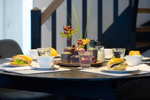 A table set with sandwiches, cups, and a vase with flowers.