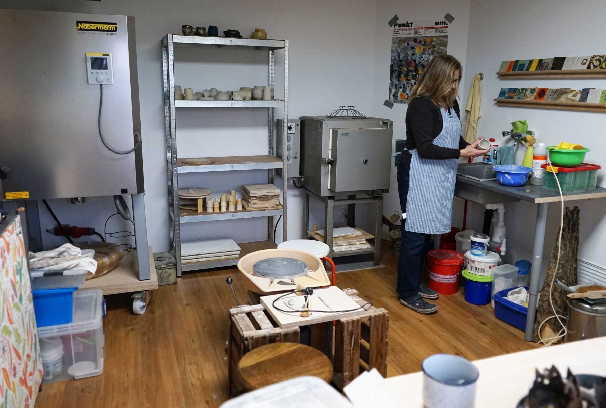 A kitchen with a bread machine, shelves with kitchenware, and a person preparing food.