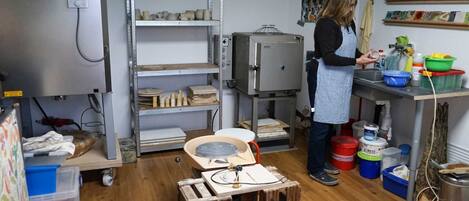A kitchen with a bread machine, shelves with kitchenware, and a person preparing food.