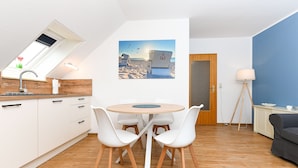 A modern kitchen with white cabinets, a skylight, and a dining area with a round table and white chairs. - Vacation apartment Gänseblümchen - Holiday apartments on the Schmidt farm (Paderborn)