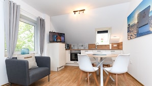 A compact kitchen with a dining area, a sofa, and a TV. - Vacation apartment Gänseblümchen - Holiday apartments on the Schmidt farm (Paderborn)