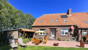 A brick house with a patio, outdoor furniture, and a small garden. - Vacation apartment Gänseblümchen - Holiday apartments on the Schmidt farm (Paderborn)
