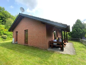 En murstensbygning med overdækket terrasse, parabolantenne og bænk.