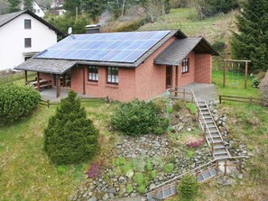 Una casa con techo solar, terraza de madera y un sendero de piedras que lleva a un columpio.