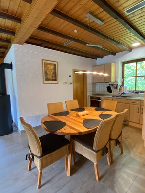 Un comedor con una mesa de madera y sillas tejidas, una pared de ladrillo blanco y una ventana con vistas a la vegetación.