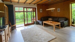 Un vaste espace de vie doté d’un plafond en bois, d’un canapé en cuir noir, d’une table basse en bois et d’une grande porte-fenêtre coulissante donnant sur un balcon.