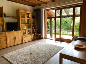 Amplia sala de estar con televisor, armarios de madera, un tapete grande y vistas a través de un ventanal.