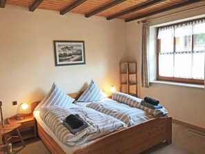 Une chambre à coucher avec un lit en bois, une table de chevet, une lampe de chevet, une fenêtre avec des rideaux et un tableau encadré au mur.