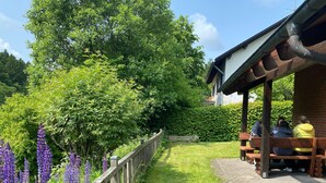 Un espace extérieur aménagé, abrité et doté d’une clôture en bois et d’un chemin dallé.