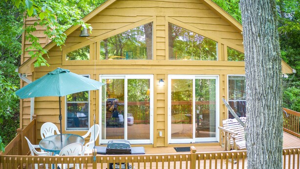 A wooden deck with a table and chairs, a covered umbrella, and a view of the surrounding trees.