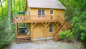 A wooden cabin with a deck, outdoor seating, and a staircase leading to the main floor.