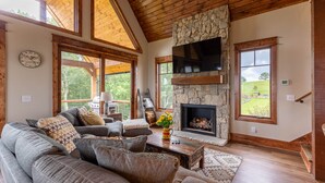 A cozy living room with a stone fireplace, large windows, and a comfortable seating area.
